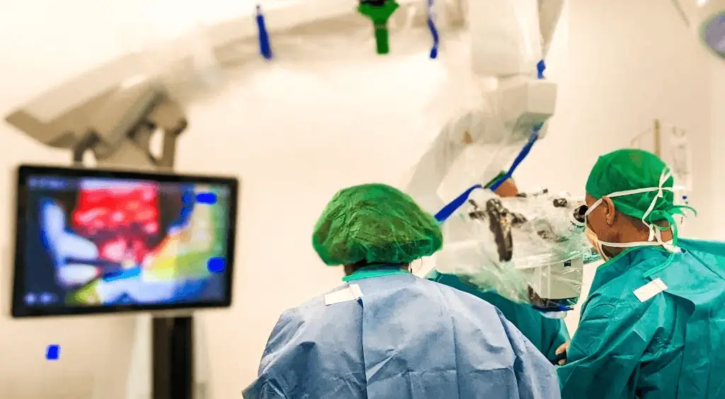 Equipo médico realizando cirugía neuroquirúrgica con microscopio y asistencia por imagen en monitor