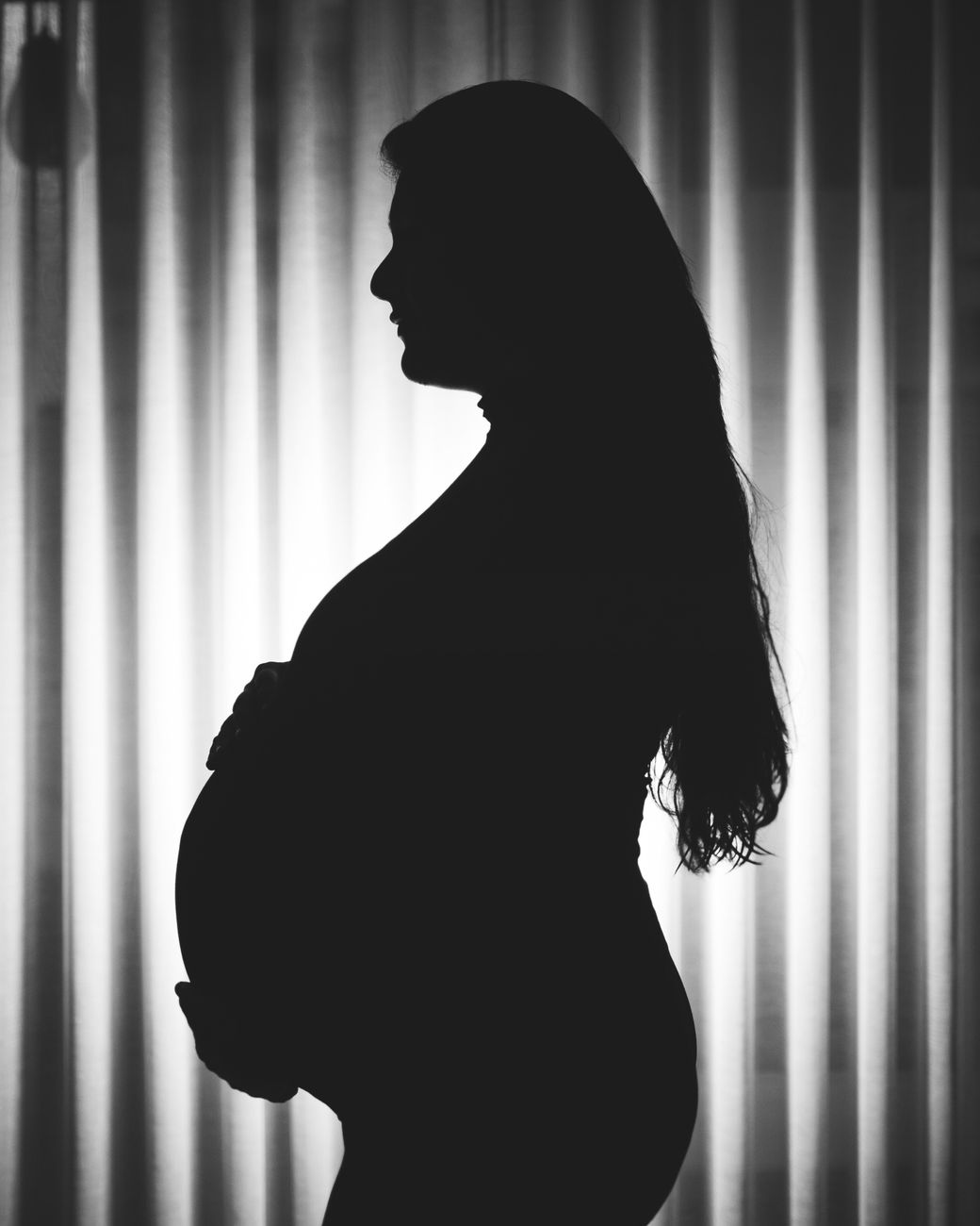 Mujer embarazada de perfil sujetándose la zona lumbar con la espalda curvada