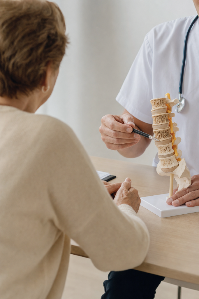 Médico mostrando una columna lumbar anatómica a una paciente en consulta