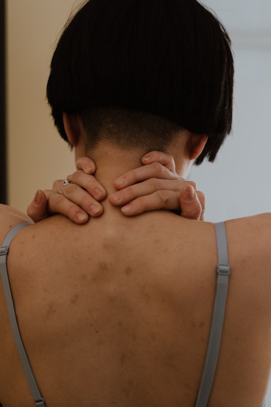 Vista posterior de cuello y espalda con postura encorvada y manos sujetando la nuca